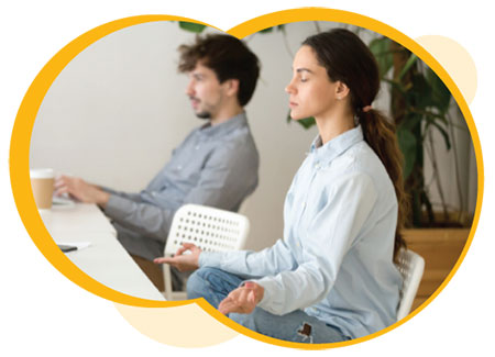 A woman meditating in an office space with a coworker in the background
